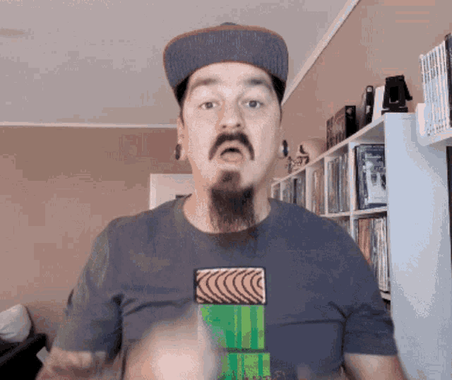 a man with a beard wearing a hat and a t-shirt with a green block on it