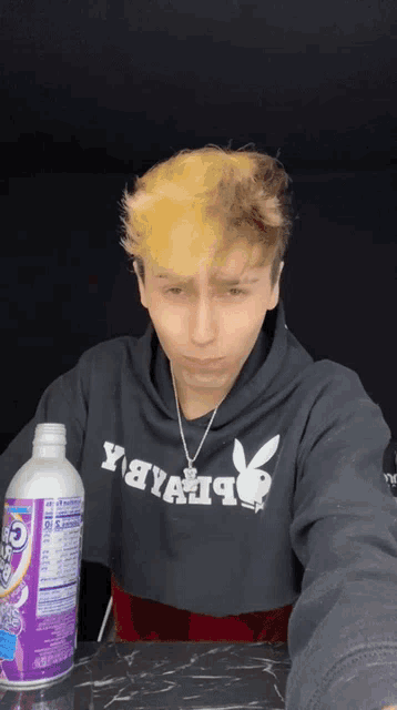 a young man wearing a playboy hoodie holds a bottle of soda
