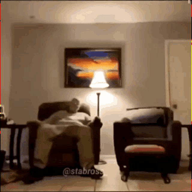 a man laying in a chair in a living room with a lamp and a painting on the wall