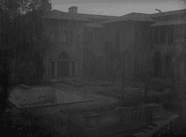 a black and white photo of a large house with a pool