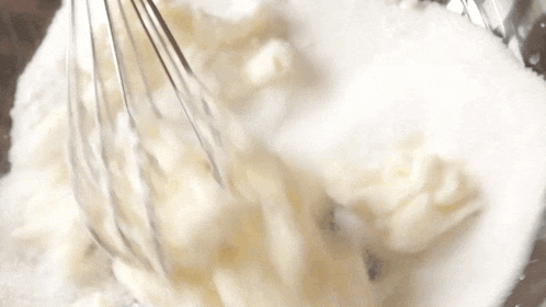 a whisk is being used to mix powdered sugar and whipped cream in a bowl .