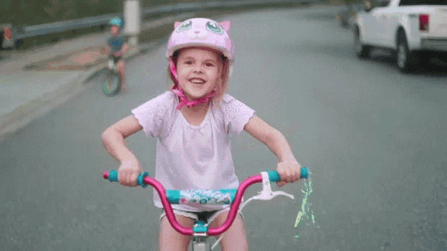 a little girl wearing a helmet is riding a bicycle down a street .