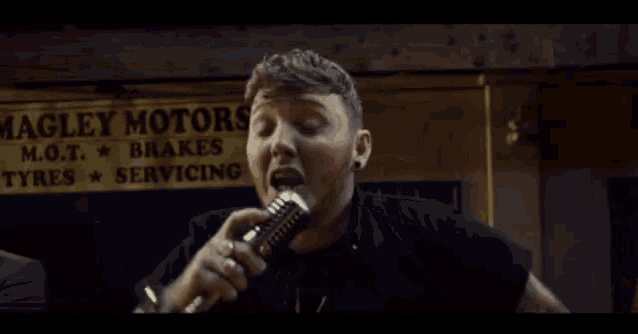 a man singing into a microphone in front of a ley motors sign
