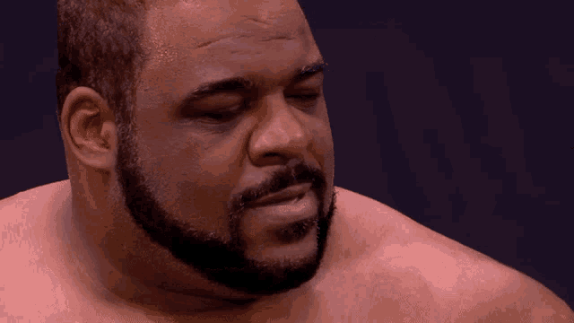 a shirtless man with a beard looks down at something