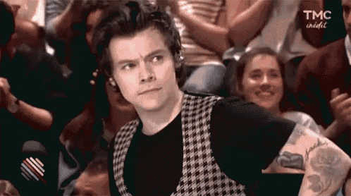 a man with a tattoo on his arm is sitting in a crowd of people and making a funny face .