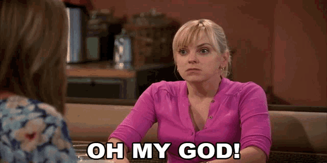 a woman in a pink shirt says oh my god while sitting at a table