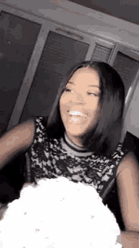 a woman in a black dress is holding a cake and smiling .