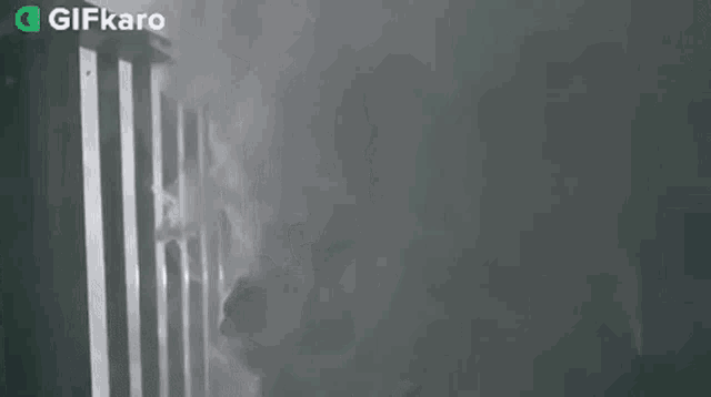 a man is holding a gun in front of a fence in a dark room .
