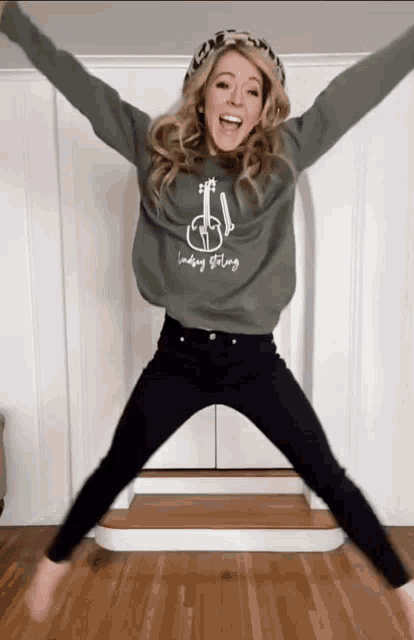 a woman is jumping in the air wearing a green sweatshirt that says leading strong