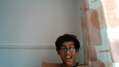 a young boy wearing glasses is smiling in front of a white wall