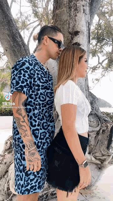 a man kissing a woman on the cheek while standing next to a tree .