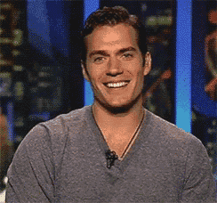 a man in a gray shirt is smiling and talking into a microphone .