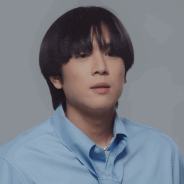 a young man wearing a blue shirt with a pearl necklace
