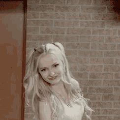 a woman is standing in front of a brick wall with her hair blowing in the wind and making a funny face .