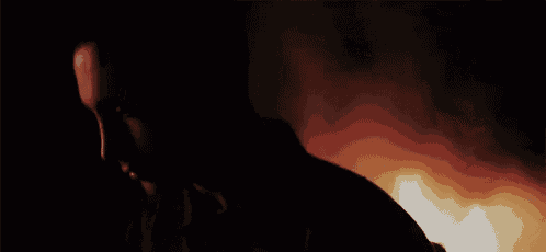 a man is standing in the dark in front of a fire