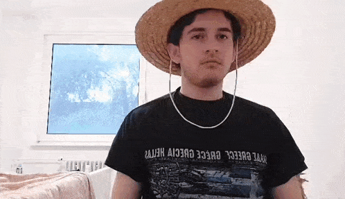 a man wearing a straw hat and a black t-shirt is standing in front of a window in a room .