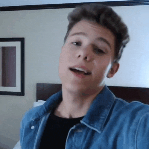 a young man is taking a selfie in a hotel room while wearing a denim jacket .