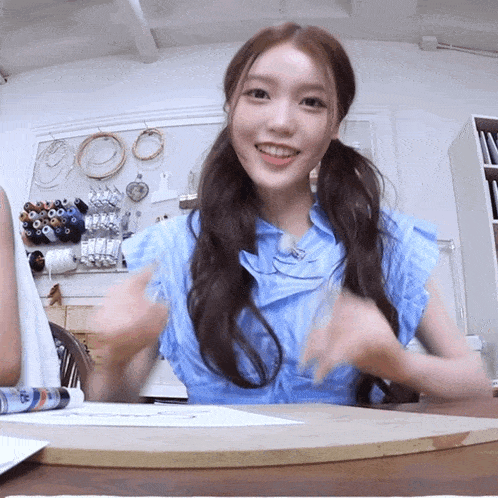 a girl in a blue shirt is sitting at a table with her hands in the air
