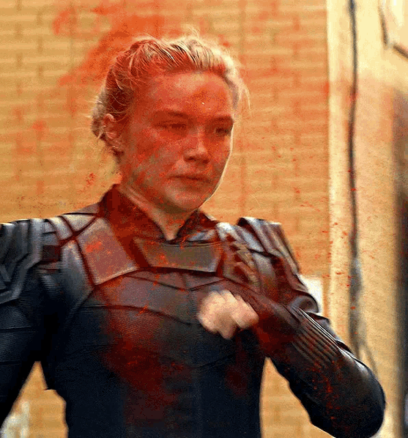 a woman is standing in front of a brick wall with blood on her face .