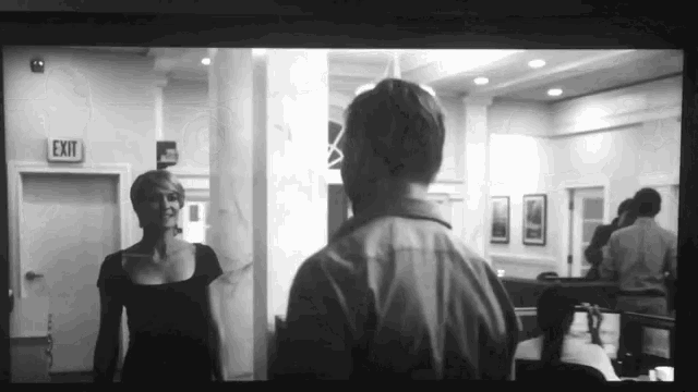 a black and white photo of a man and a woman in front of an exit sign