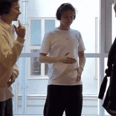 a man wearing headphones is standing in front of a window with his hand in his pocket