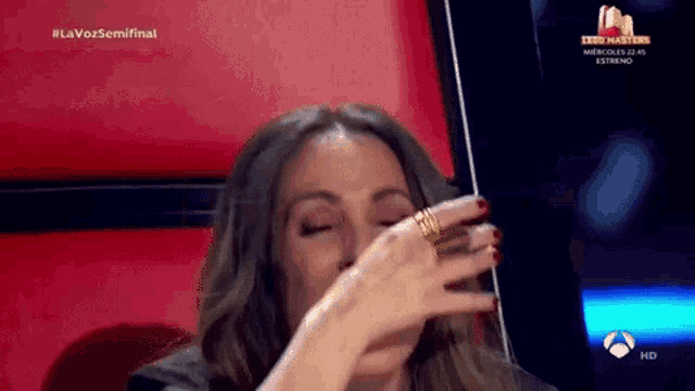 a woman is covering her face with her hand while sitting in a chair on a tv show .