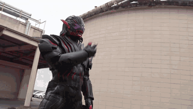 a man in a black costume is standing in front of a brick building