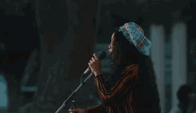 a woman wearing a plaid hat singing into a microphone
