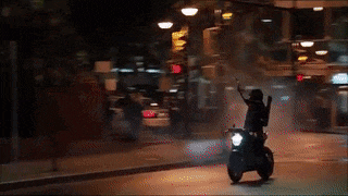 a person riding a motorcycle down a street with a gun in their hand