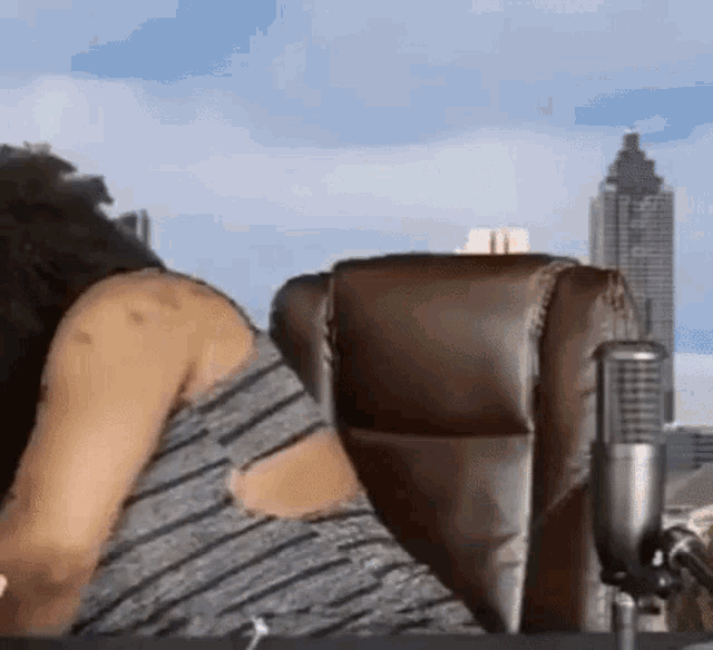 a woman is sitting in a chair in front of a microphone in front of a city skyline .