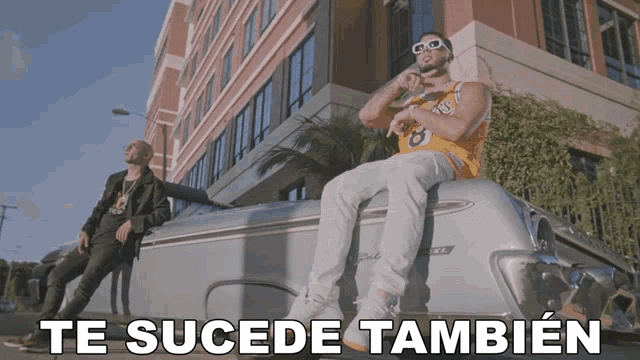 a man in a lakers jersey sits on the back of a silver car