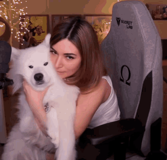 a woman is hugging a white dog in front of a secret lab chair