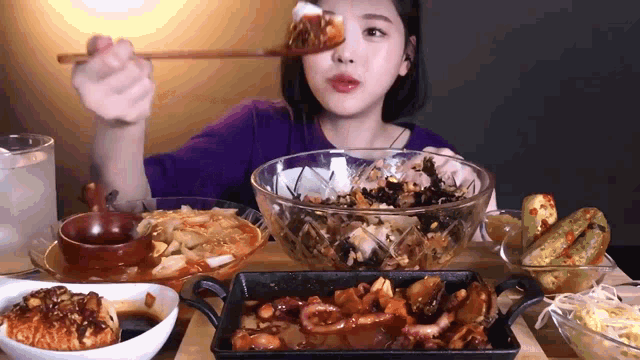 a woman is sitting at a table eating a bowl of food with chopsticks .