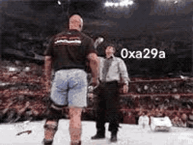 a man in a black shirt and blue shorts is standing in a boxing ring with a referee .