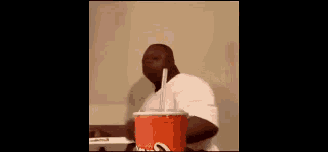 a man is drinking from a cup with a straw .