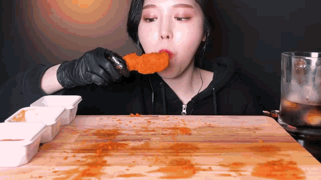 a woman wearing black gloves is eating a piece of fried food