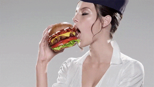 a woman wearing a chef hat is biting into a hamburger