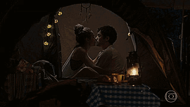 a man and woman are kissing in a tent with a lantern