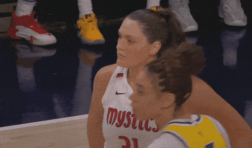 a basketball player wearing a mystics jersey talks to another player
