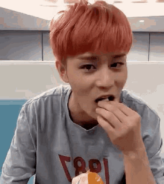 a young man with red hair is eating an orange while wearing a gray shirt .