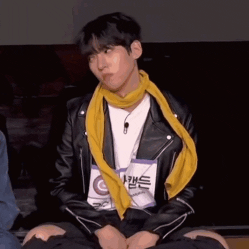 a young man wearing a leather jacket and a yellow scarf is sitting on the floor .