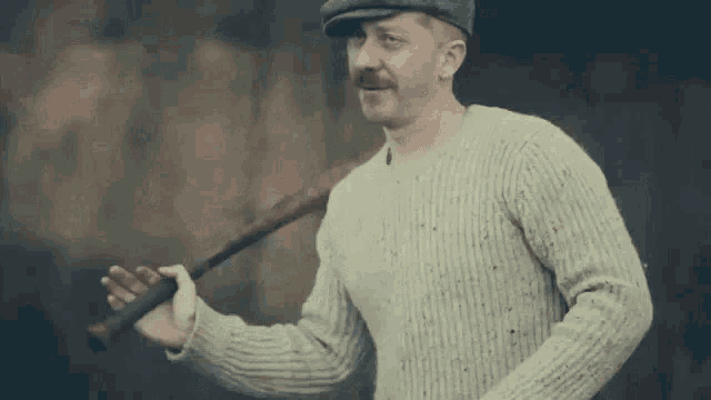 a man in a sweater and hat is holding a baseball bat in his hand .
