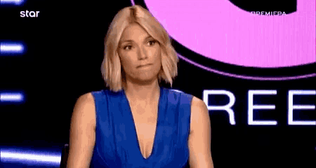 a woman in a blue dress is sitting in front of a pink background with the word ree on it .