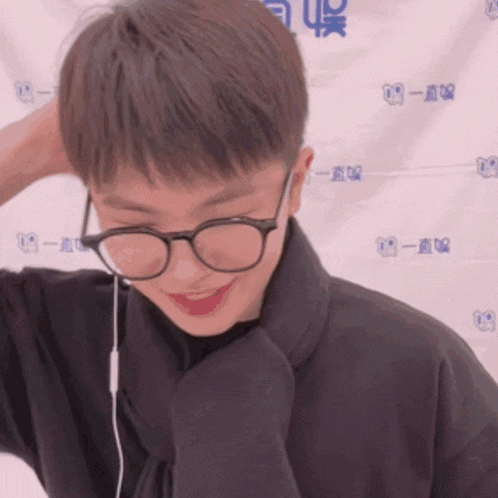 a man wearing glasses and a scarf is smiling in front of a wall with chinese characters on it