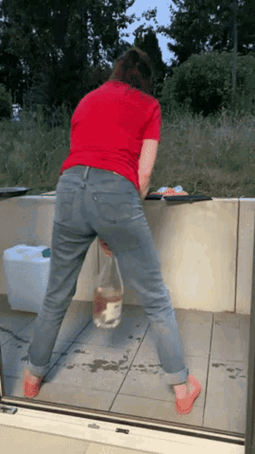 a woman in a red shirt and blue jeans is standing on a tiled floor