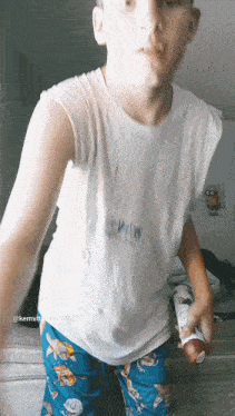 a boy wearing a white tank top and blue pajama pants is holding a bottle