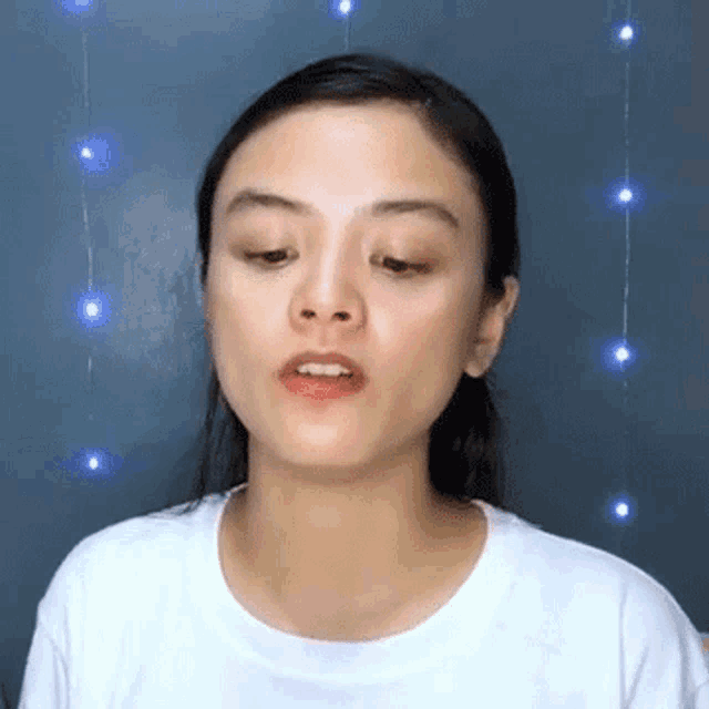 a woman in a white shirt is making a funny face in front of a string of lights .