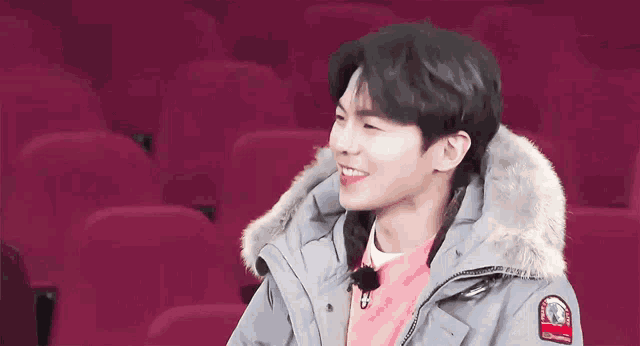 a young man wearing a grey jacket with a fur hood is sitting in a stadium .