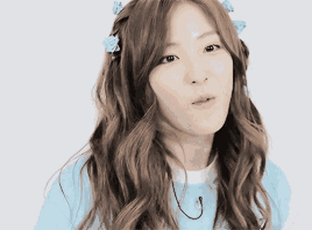 a woman with long wavy hair wearing a blue shirt and a flower in her hair