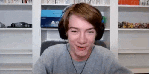a young man wearing headphones is making a funny face while sitting in front of a bookshelf .
